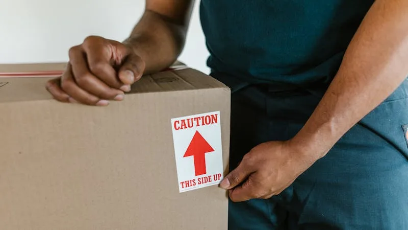 Person carefully carrying a labeled moving box