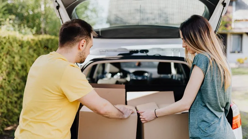 A couple loading moving boxes into the trunk of a car